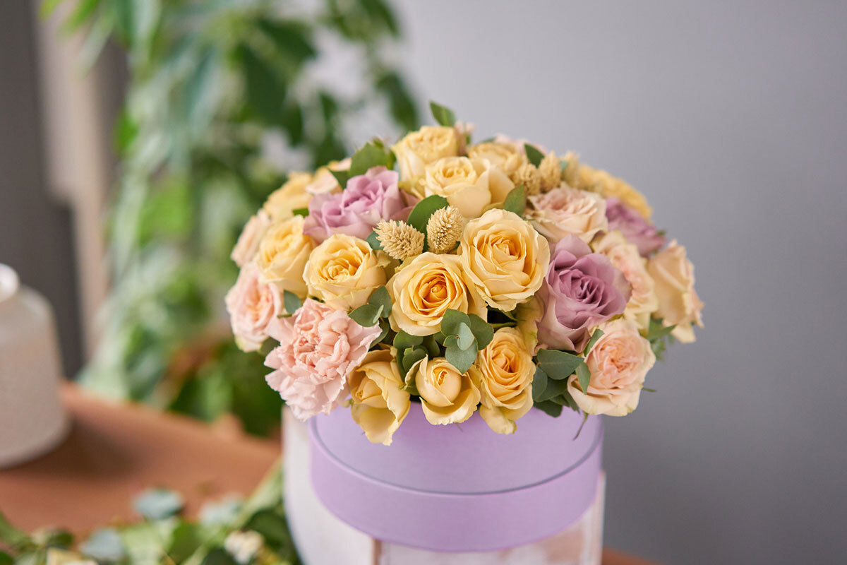 A bouquet of yellow roses with purple roses inside the circular purple box.