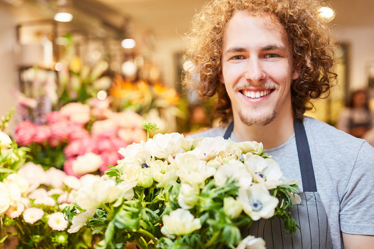 A young florist smiling in flower shop with fresh flowers for customers