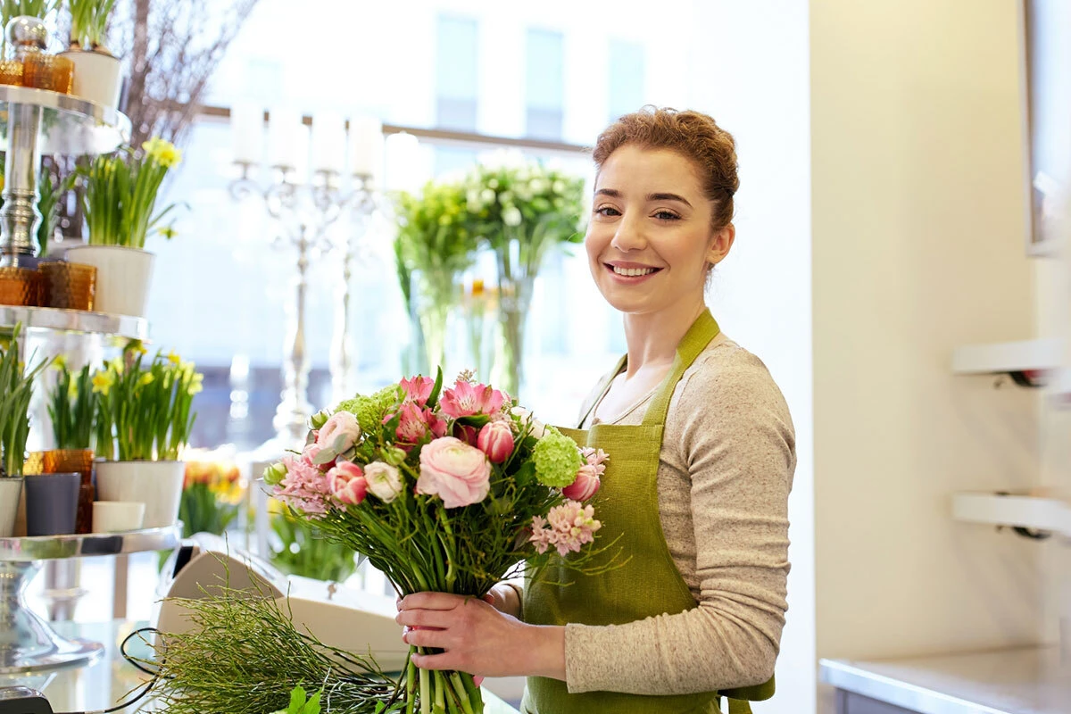 A young florist smiling while preparing holding a bouquet for client
