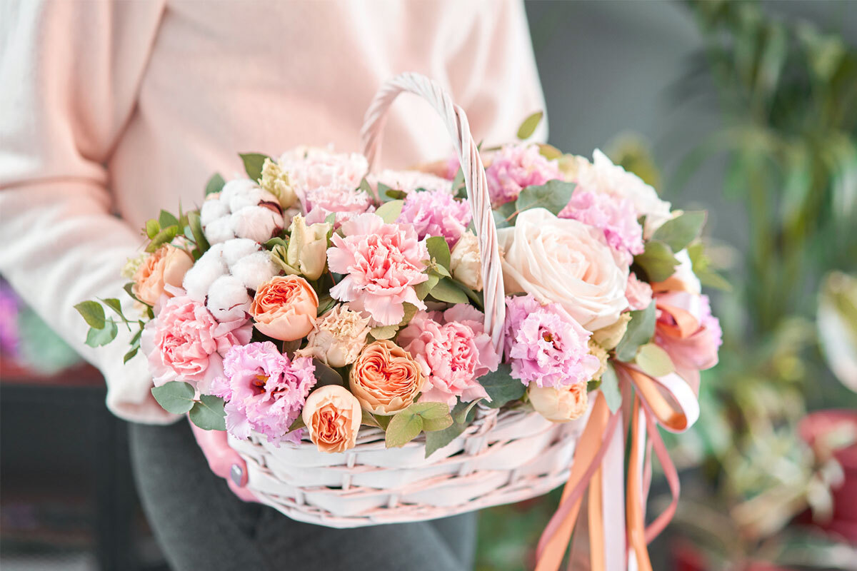 A woman holding a baskets of vibrant pink and white flowers