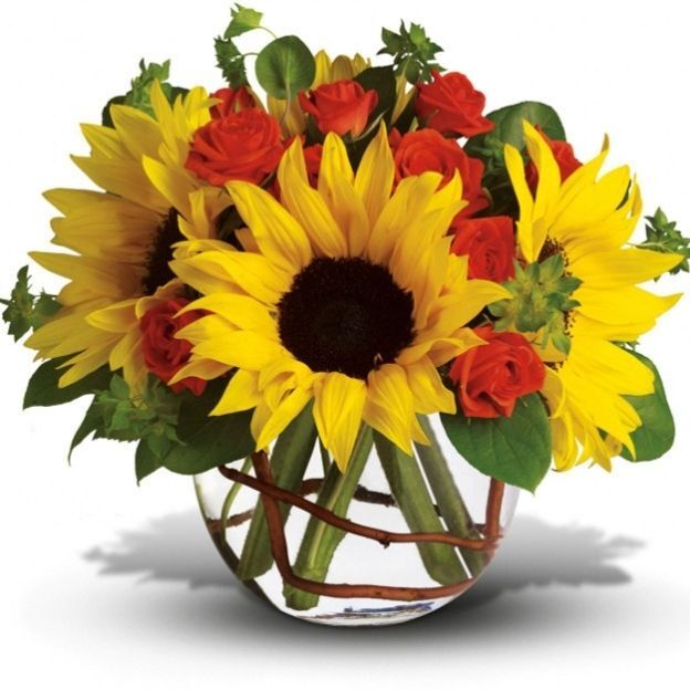 Bright floral arrangement featuring sunflowers, roses, and mixed greenery in a clear glass vase.