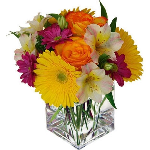 Bright bouquet in a clear cube vase with yellow gerberas, orange roses, magenta daisies, and soft pink alstroemeria.