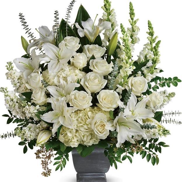 Large bouquet of white flowers including lilies, roses, and snapdragons with lush green leaves in a decorative vase.