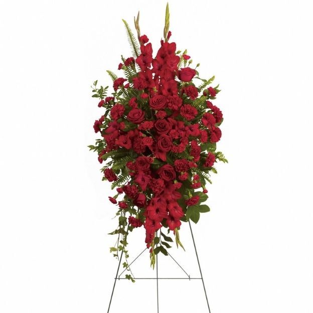 Elegant red floral arrangement on a stand, featuring roses, carnations, gladiolus, and greenery