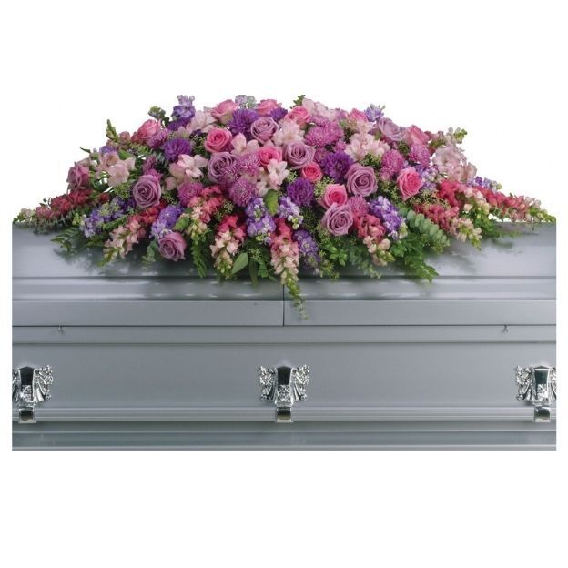 Casket spray of pink, purple, and lavender flowers including roses, snapdragons, and greenery on a silver casket.