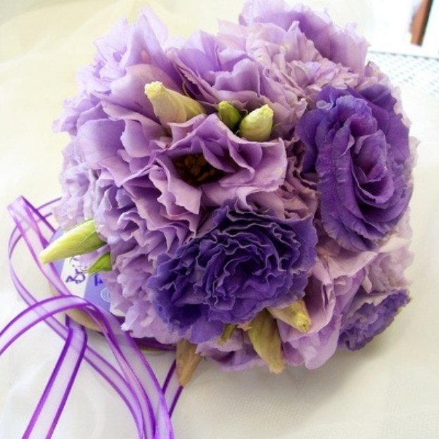 Elegant purple floral bouquet featuring layered lisianthus blooms with green buds and ribbon accents.