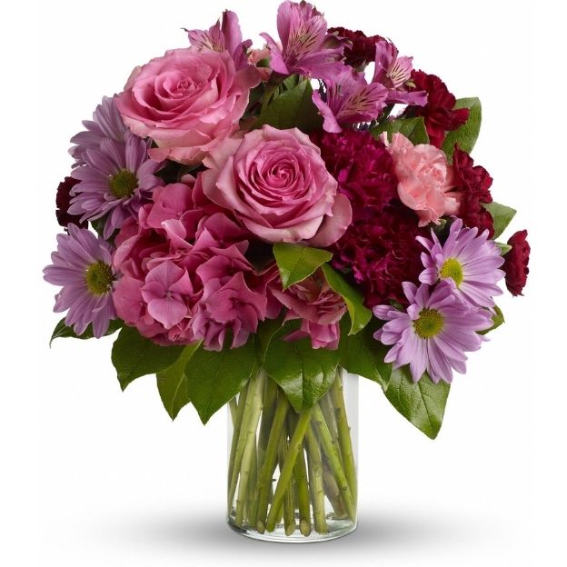 Vibrant mix of pink and purple flowers, including roses and daisies, in a clear glass vase with visible green stems.