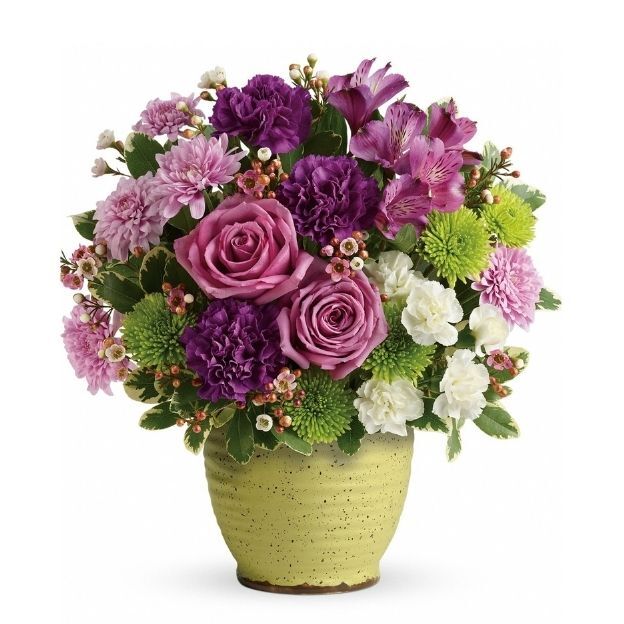 A yellow vase filled with purple roses, carnations, green button poms, white mini carnations, and pink flowers.