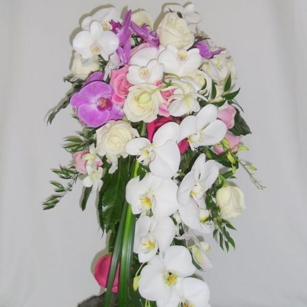 Elegant floral arrangement featuring white orchids, pale yellow roses, pink roses, and lush green leaves.
