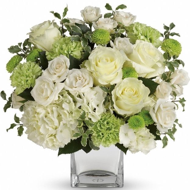 Elegant bouquet of white roses, hydrangeas, and green carnations in a clear square glass vase.