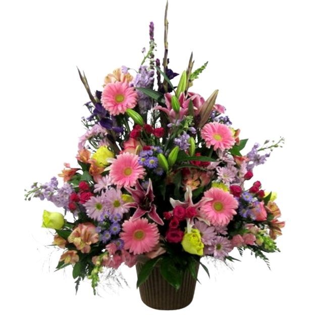 Sympathy-style arrangement featuring pink daisies and lilies with red roses, lavender blooms, and lush foliage.