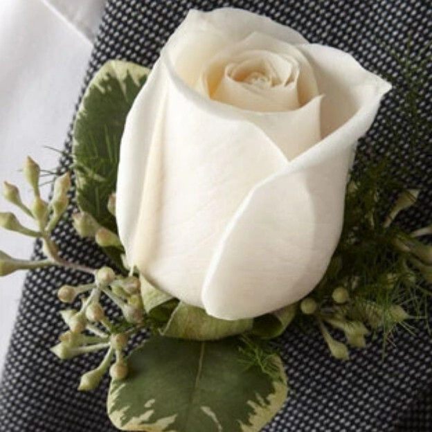 White rose boutonniere with cream-edged green leaves and small pale buds pinned to a black-and-white textured lapel.