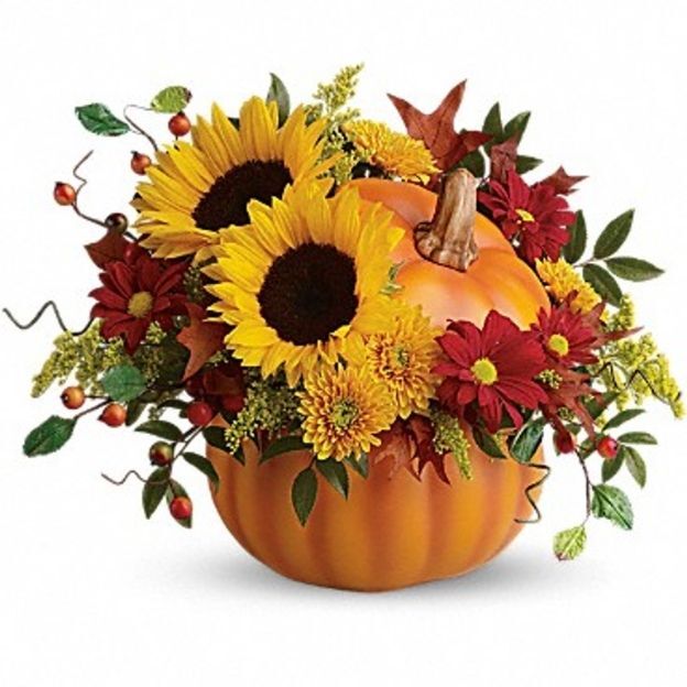 Pumpkin vase with sunflowers, red mums, yellow mums, berries, and fall leaves in a festive autumn arrangement.